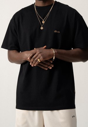 Czarny bawełniany t-shirt z okrągłym dekoltem i haftowanym logo, w zestawieniu z beżowymi siateczkowymi szortami. Uzupełniony o złote naszyjniki warstwowe i pierścionki.