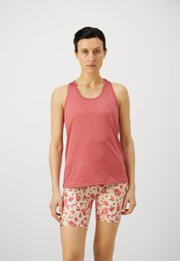 Rotes Tanktop mit Rundhalsausschnitt und ärmellosem Design, kombiniert mit cremefarbenen Shorts mit floralem Muster, die rosa und rote Blumen zeigen.