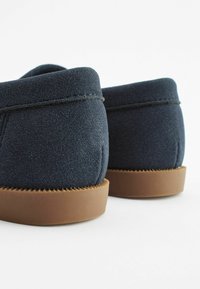 Marinblå ruskindssko med en brun gummisål, der har en glat tekstur og afrundet rygdesign. Kantsting langs kanterne.