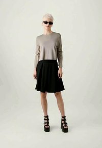 Top bege de manga longa, saia preta godê e sandálias pretas de plataforma chunky. O modelo usa óculos de sol pretos e elegantes. Design simples e moderno.