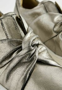 Metallic silver shoes made of textured material featuring a knotted design on the front and a smooth, rounded shape.