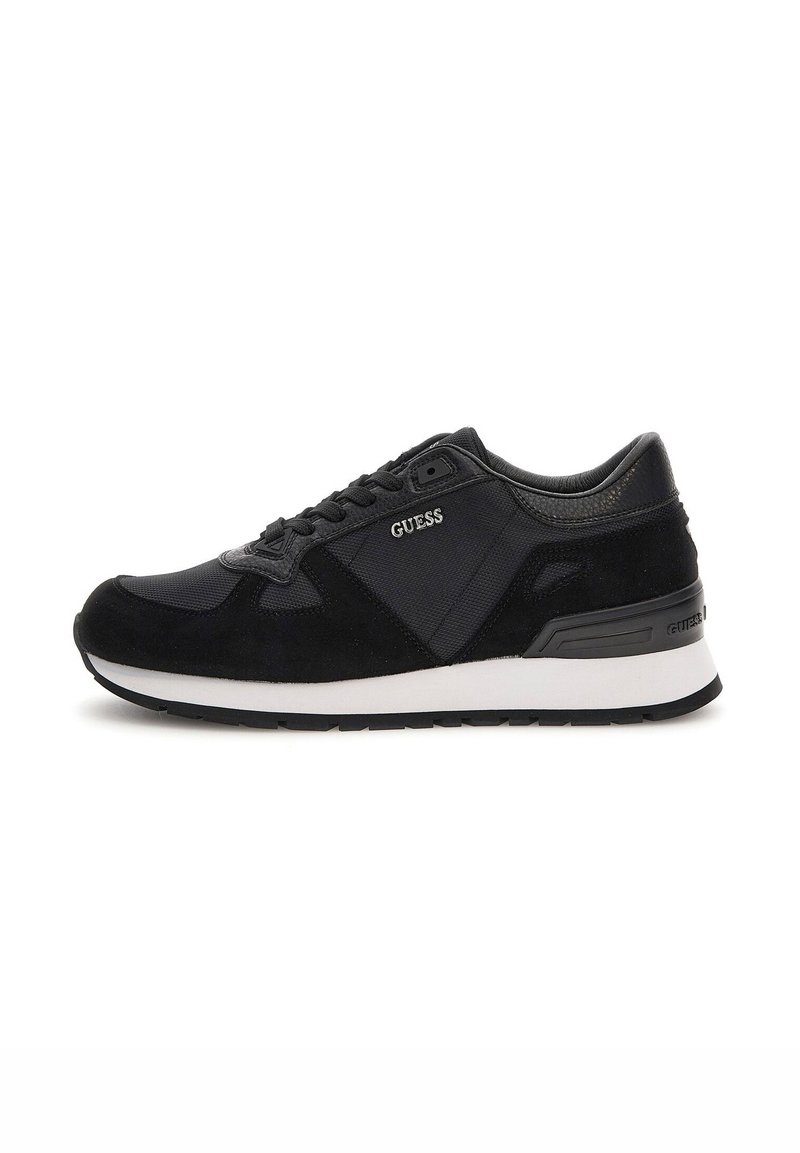 Chaussure de sport noire avec un mélange de matériaux lisses et texturés, dotée d'une semelle intermédiaire blanche, d'un système de laçage et du logo « Guess » sur le côté.