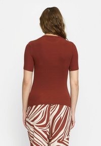 Roestkleurige geribbelde top met korte mouwen en een aansluitende vorm, gecombineerd met beige broek met opvallende bruine zebrapatronen. Achteraanzicht weergegeven.