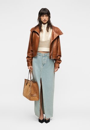 Veste courte en cuir marron, pull en tricot crème, jupe en denim bleu clair avec une fente, sac à main en daim marron et talons noirs.