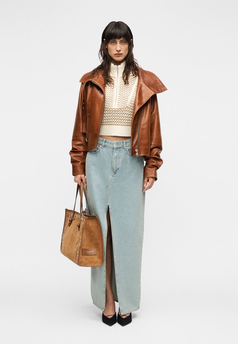 Καφέ δερμάτινο κοντό μπουφάν, κρεμ πλεκτό πουλόβερ, φούστα τζιν ανοιχτού μπλε με σκίσιμο, καφέ τσάντα από σουέντ και μαύρες γόβες.