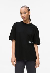 Sort oversized t-shirt lavet af bomuld med korte ærmer og rund halsudskæring, med hvid broderet branding på venstre side.
