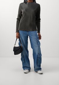 Top a maniche lunghe nero a coste, jeans cargo blu con tasche, sneakers bianche e una piccola borsa nera. Texture liscia e vestibilità rilassata.