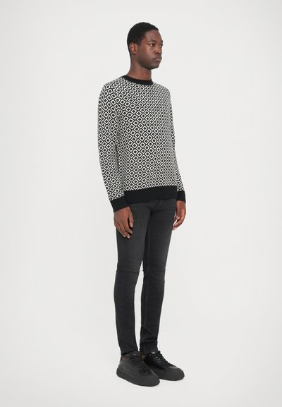 Black and white patterned sweater with a round neck and long sleeves, paired with slim-fit black jeans and black sneakers.