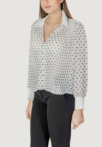 Camicia bianca con pois neri, design plissettato, chiusura con bottoni frontale e maniche lunghe; presenta un colletto classico e polsini a contrasto.