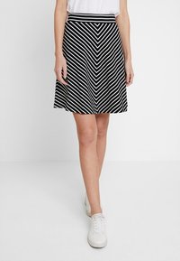 Musta-valkoinen wego-toimikukoilla varustettu hame, jossa on istuva vyötärö, levenevä muoto ja sileä pinta, yhdistettynä valkoisiin lenkkareihin.