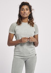 Lys grå sports top med korte ærmer, der har teksturerede detaljer på skuldrene og ribbet kant. Materialet ser blødt og strækbart ud.