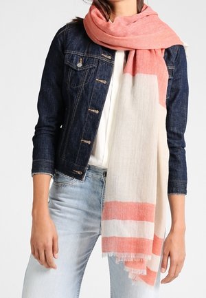 Femme portant une veste en jean foncé et un jean bleu clair avec une grande écharpe rayée rose et crème enroulée autour du cou.