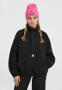 Crni fleece pulover s visokim ovratnikom i elastičnom gumom, s trokutastim logotipom. Rozi rebrasti šešir s logotipom.