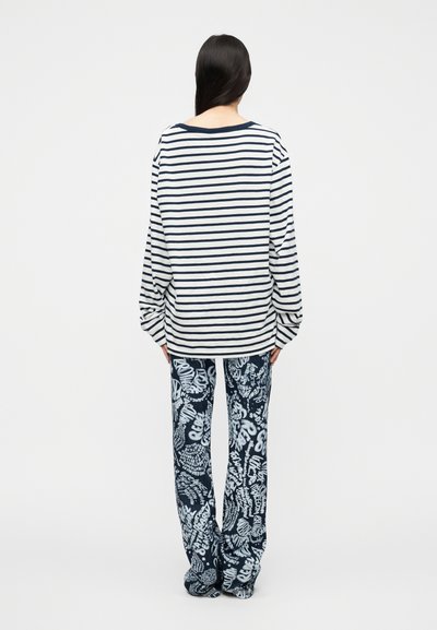 Μπλούζα μακρυμάνικη με ρίγες σε ναυτικό μπλε και λευκό; συνδυασμένη με παντελόνι φαρδύ στο πόδι με μπλε και λευκό αφηρημένο μοτίβο. Σετ casual ρούχων για χαλάρωση.