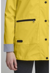 Yellow rain jacket made of waterproof material, featuring a black zippered pocket, snap closures, and striped cuff details.