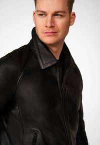 Black leather motorcycle jacket with a high collar, zip closure, and side pockets. Smooth texture, fitted design, and minimal stitching details.