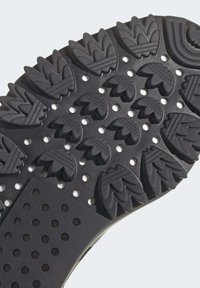 Svart gummisul med ett texturerat mönster som har upphöjda bladliknande former och perforeringar för grepp och flexibilitet.