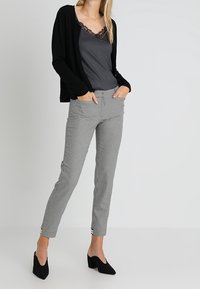 Svart cardigan över en grå linne med spetskant, i kombination med grå och svarta rutiga byxor och svarta klackskor. Minimalistisk design.