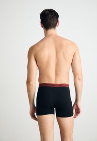 Black boxer shorts with a red waistband featuring "BJÖRN BORG" logo. Smooth texture and fitted design, seen from the back.