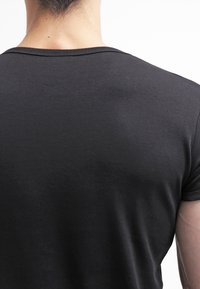 Camiseta de algodón negra vista desde la parte posterior, con un cuello redondo y mangas cortas, con una textura suave y detalles de diseño mínimos.