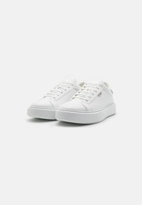 Zapatillas deportivas blancas con un upper de cuero texturizado, cordones planos, un talón reforzado y una suela de goma gruesa con un diseño minimalista.
