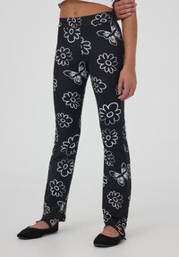 Pantaloni elasticizzati neri con un motivo floreale bianco e disegni di farfalle, con una silhouette aderente e una vita elastica.
