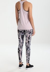 Top de tirantes en rosa claro combinado con leggings de tiro alto con un patrón de mármol negro y en tonos pastel. Zapatillas deportivas negras.