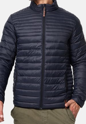 Navy blue padded jacket featuring vertical quilted texture, a stand collar, full front zipper, and logo accent near the hem.