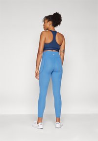 Leggings blu con vita alta, realizzati in tessuto elasticizzato e con un design aderente. Abbinati a un reggiseno sportivo blu navy, con schiena a scoperta.