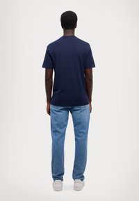 Marineblauwe katoenen t-shirt met korte mouwen en een ronde hals, gecombineerd met lichtblauwe denim jeans en witte sneakers.