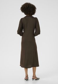 Rochie lungă, de culoare maro, cu mâneci bufante și decolteu rotund, având o siluetă fluidă și tiv până la genunchi. Asortată cu încălțăminte în dungi negre și albe.