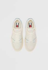 White leather sneakers with perforated details, light blue accents, and white laces. Features a branded tongue label with red and blue stripes.