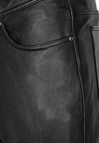Zwarte leren broek met een gladde textuur, zijzakken en contrasterende stiksels. De stof lijkt duurzaam en gestructureerd.