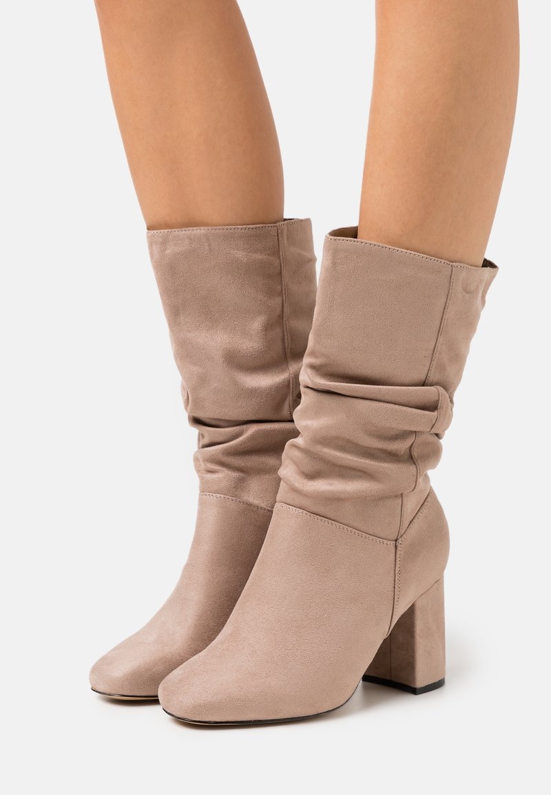 Beige slouch ankle boots with a textured suede material, square toe, and a chunky block heel for stability.