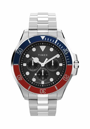 Ezüst színű Timex karóra fekete számlappal, piros és kék lünettával, három segédszámlappal, amelyek a napot, a 24 órás időt és az stopperfunkciókat mutatják.