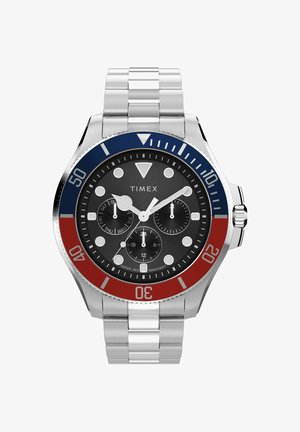 Srebrny metalowy zegarek Timex na rękę z czarną tarczą, czerwono-niebieskim bezelem oraz trzema małymi tarczami wskazującymi dzień, czas w formacie 24-godzinnym i funkcję stopera.