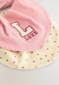 Bavoir en coton avec un dessus en ribbi rose portant un "L" et "amour" en broderie. Le dessous est jaune avec de petits motifs floraux roses.