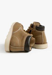 Stivaletti in pelle marrone con accenti neri sul tacco, lacci gialli, cuciture bianche e suola in gomma. Cerniera laterale per una facile vestibilità.