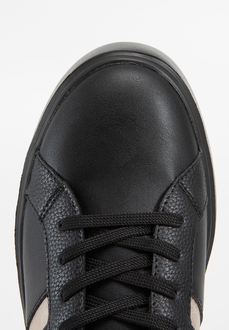 Baskets noires en cuir lisse avec des accents texturés, dotées de lacets noirs et d'une semelle gris clair. Design minimaliste avec des éléments contrastés.