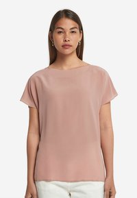 Rosa blus med kort ärm, gjord av lätt och slät tyg. Har en bred halsringning och en avslappnad passform, fållen slutar precis under midjan.