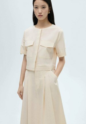 Chemise rose pêche raccourcie à manches courtes avec deux poches poitrine, assortie d'une jupe taille haute à plis.