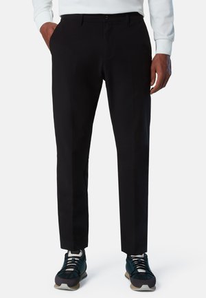 Sorte bukser med lige pasform, lavet af glat stof. Har forlommer og lynlåsgylp, kombineret med atletisk fodtøj.