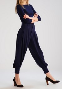 Námořnické modré haremové kalhoty s vysokým pasem, záhyby a elastickými manžetami, v kombinaci s černými botami na vysokém podpatku s želvovinovým vzorem.