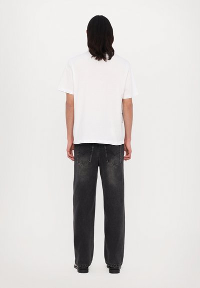 T-shirt blanc à manches courtes associé à un jean gris foncé à coupe ample. La tenue présente un design décontracté avec des détails de couture visibles.
