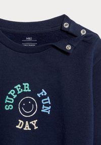 Granatowa bluza z okrągłym dekoltem, zapięcie na guziki na ramieniu oraz kolorowy haftowany tekst: "SUPER ZABAWNY DZIEŃ" z uśmiechniętą buźką.