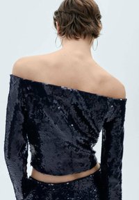 Svart paljettemönstrad off-shoulder-top med långa ärmar, figurnära design, glittrande yta och kort längd, synliga sömmar längs fållen.