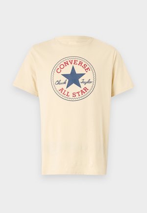 Camiseta de algodón color crema con un logo de estrella azul y texto rojo que dice "Converse Chuck Taylor All Star" en un diseño circular.