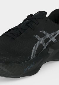 Μαύρο παπούτσι τρεξίματος ASICS με γκρι λογότυπο, μαύρα κορδόνια και παχιά σόλα με την ένδειξη "FF Turbo²" σε λευκό φόντο.
