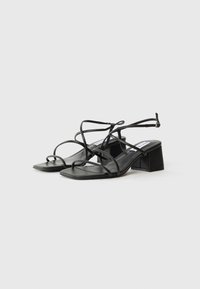 Sorte sandaler med tynne stropper, firkantet tå og blokkhel. Laget av glatt lær, med et minimalistisk design og justerbare spenn.