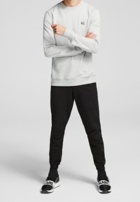 Felpa grigia chiara con maniche lunghe e scollatura rotonda, abbinata a pantaloni della tuta neri a gamba stretta. Sneakers nere con dettagli bianchi.